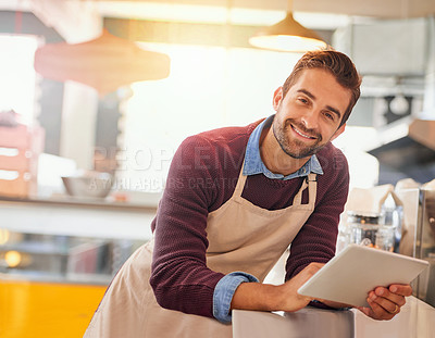 Buy stock photo Portrait of happy young business owner using a tablet while standing in his coffee shop