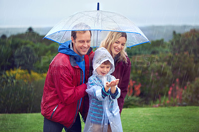 Buy stock photo Rain, umbrella and a happy family outdoor in nature for fun, happiness and quality time. Man, woman and excited child together with hands to catch water drops while learning, playing or development