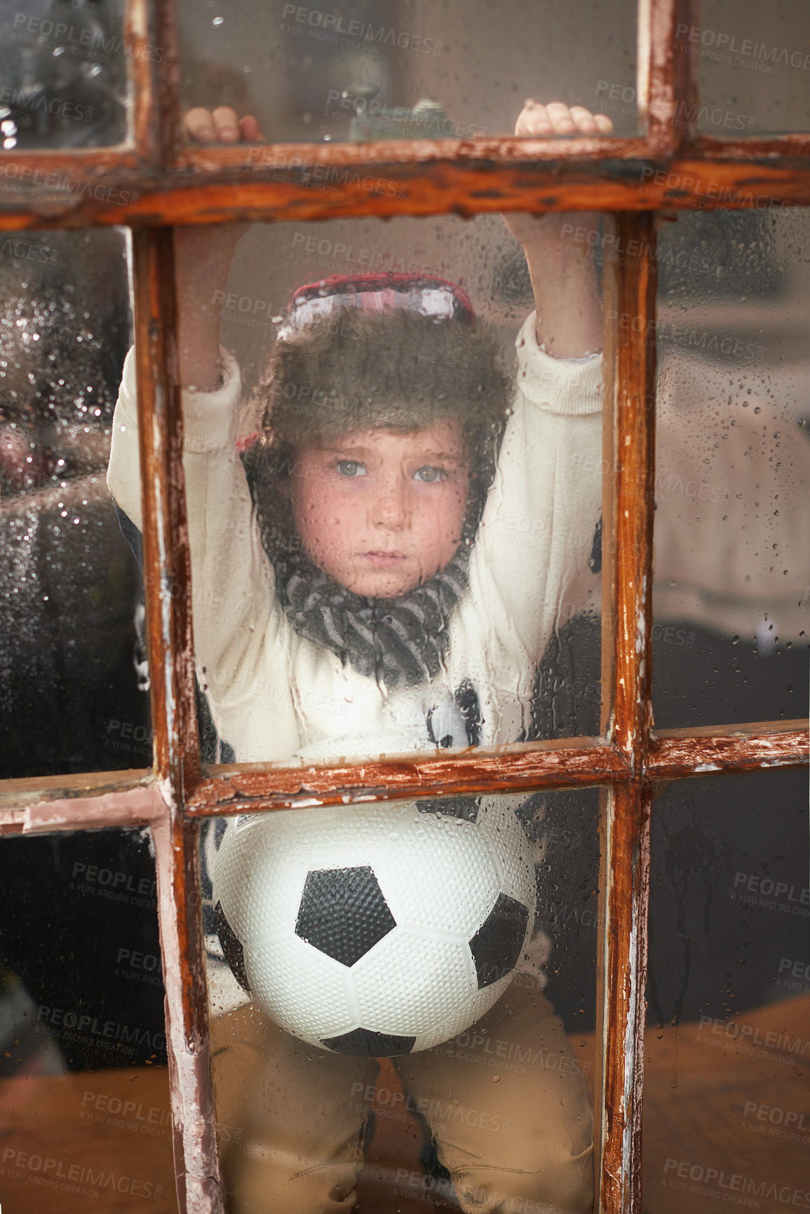 Buy stock photo Rain, window and boy with soccer ball, sad and bored with weather, cold and season. Portrait, kid and child with emotion, view or sports with glass, upset or home with thunderstorm, expression or wet