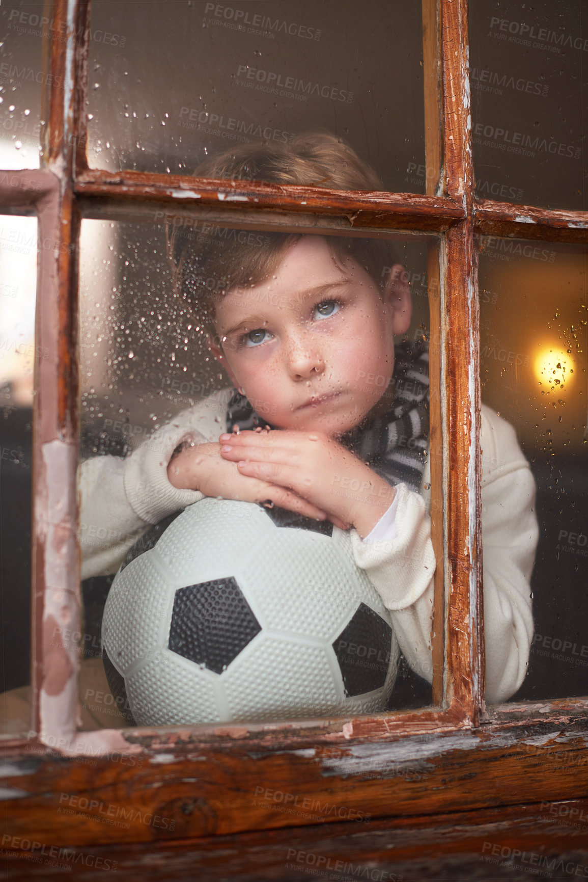 Buy stock photo Thinking, sad and kid by window with soccer ball for playing outdoor, frustrated and waiting for rain. Bored, lonely and young boy by glass with football for mental health and psychology in Ireland