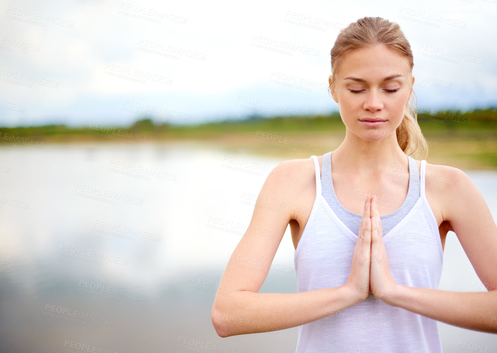 Buy stock photo Shot of a focussed young woman doing yoga next to a lake outside