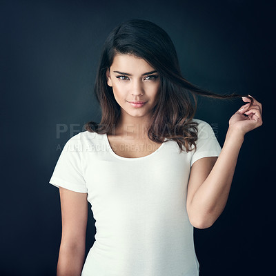Buy stock photo Studio shot of a beautiful young woman playing with her hair against a dark background