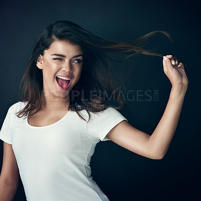 Buy stock photo Studio shot of a beautiful young woman playing with her hair against a dark background