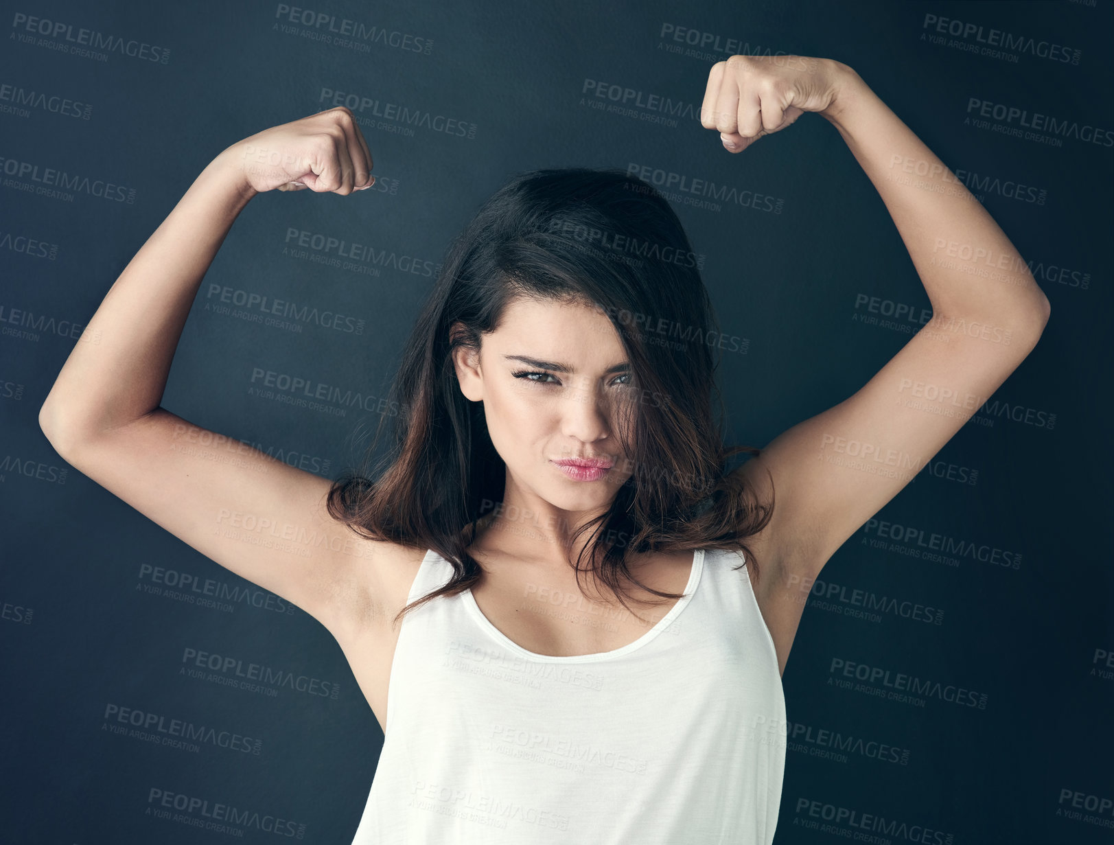 Buy stock photo Studio shot of a beautiful young woman flexing her muscles against a dark background
