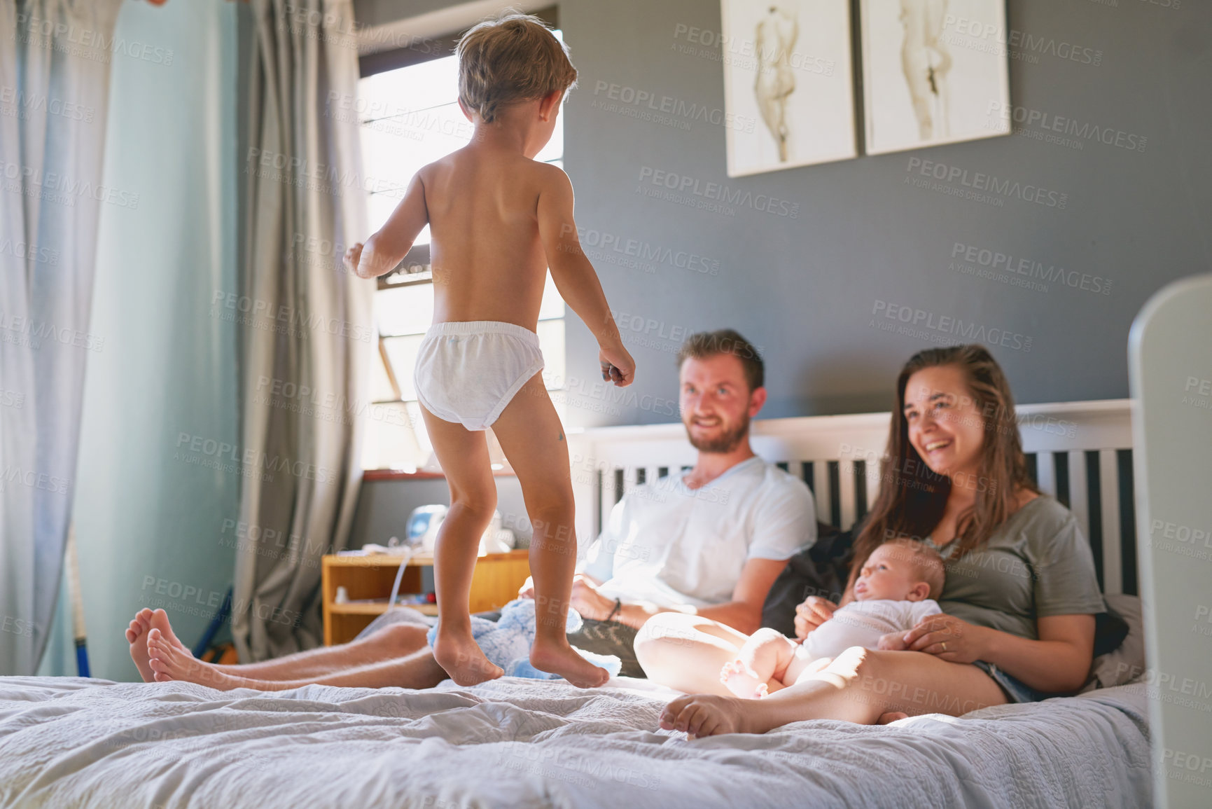 Buy stock photo Relax, parents and child jump on bed for fun, bonding and playing together in bedroom. Morning, boy and happy man with woman watching kid for comfortable, energy or lazy weekend in family home