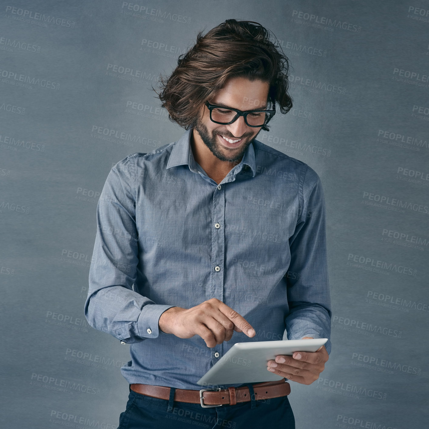 Buy stock photo Shot of a handsome young man using a digital tablet against a gray background