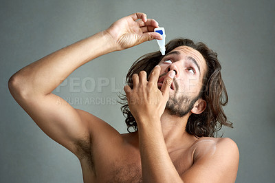Buy stock photo Studio shot of a handsome young man applying eyedrops to his eyes against a grey background