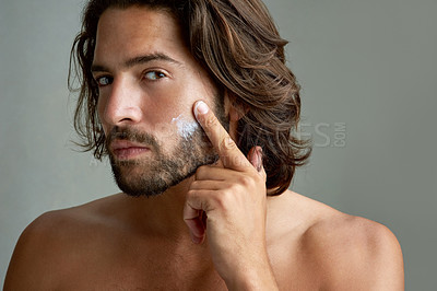 Buy stock photo Portrait, facial or lotion with a shirtless man in studio on a gray background for his grooming routine. Skincare, face and beauty with the body of a young person with antiaging cream for his skin