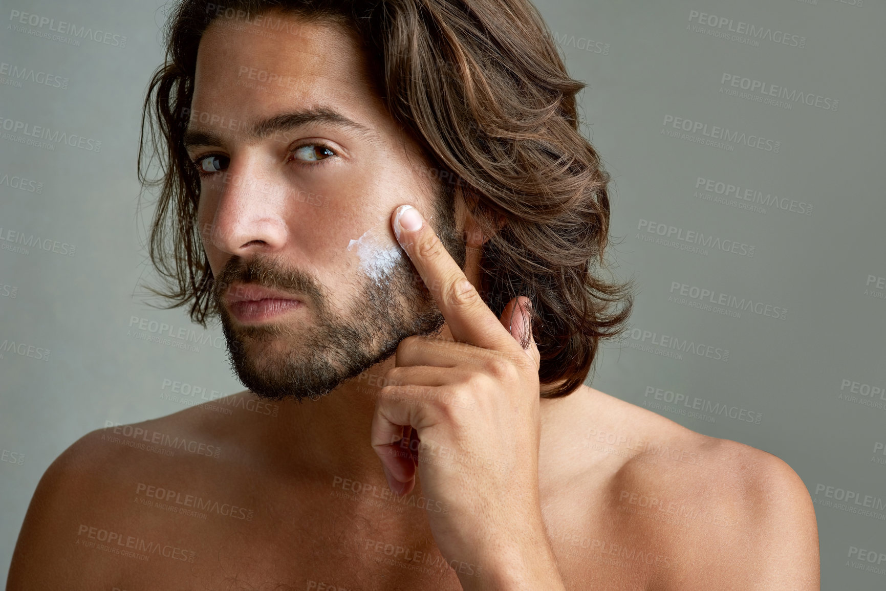 Buy stock photo Portrait, facial or lotion with a shirtless man in studio on a gray background for his grooming routine. Skincare, face and beauty with the body of a young person with antiaging cream for his skin