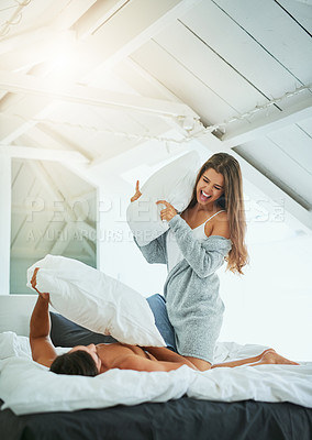 Buy stock photo Shot of a happy and playful young couple having a pillow fight in bed