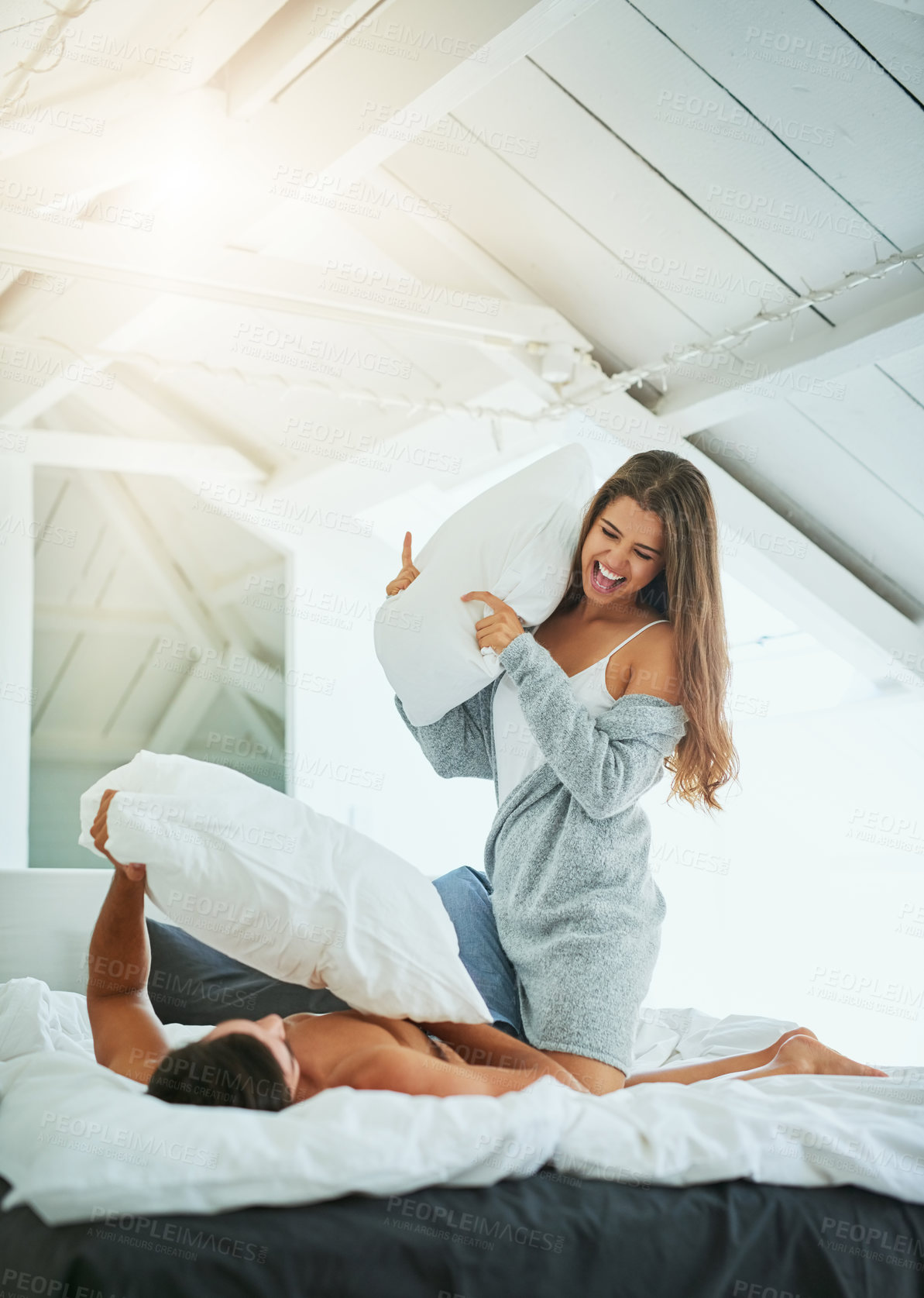 Buy stock photo Shot of a happy and playful young couple having a pillow fight in bed