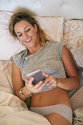 Buy stock photo Cropped shot of an attractive woman smiling and scrolling on her cellphone in bed at home