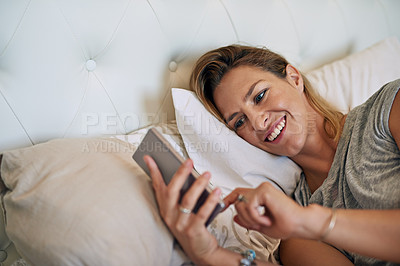 Buy stock photo Cropped shot of an attractive woman smiling and scrolling on her cellphone in bed at home