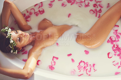 Buy stock photo Shot of a beautiful nude woman relaxing in a bathtub filled with milk and flower petals at home