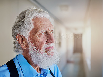 Buy stock photo Shot of a senior man looking thoughtful while standing in the hallway of his nursing home