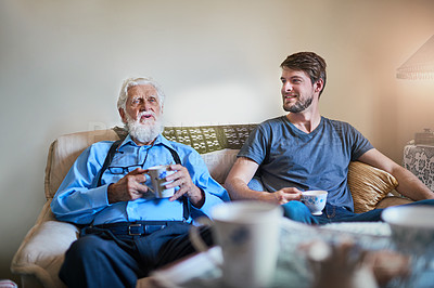 Buy stock photo Shot of a senior man and his adult grandson enjoying coffee together on the couch at home