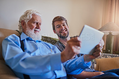 Buy stock photo Shot of a young man showing his elderly grandfather how to use a tablet while sitting on the couch at home