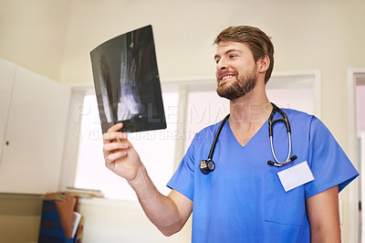 Buy stock photo Shot of a young doctor analyzing an x-ray alone in his office