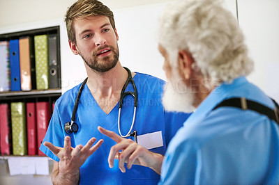 Buy stock photo Shot of a young doctor discussing his diagnosis with his senior patient in the hospital