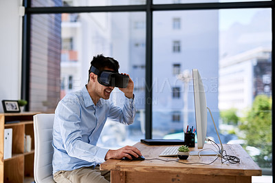 Buy stock photo Shot of a happy young businessman wearing a virtual reality headset while working at his desk in the office