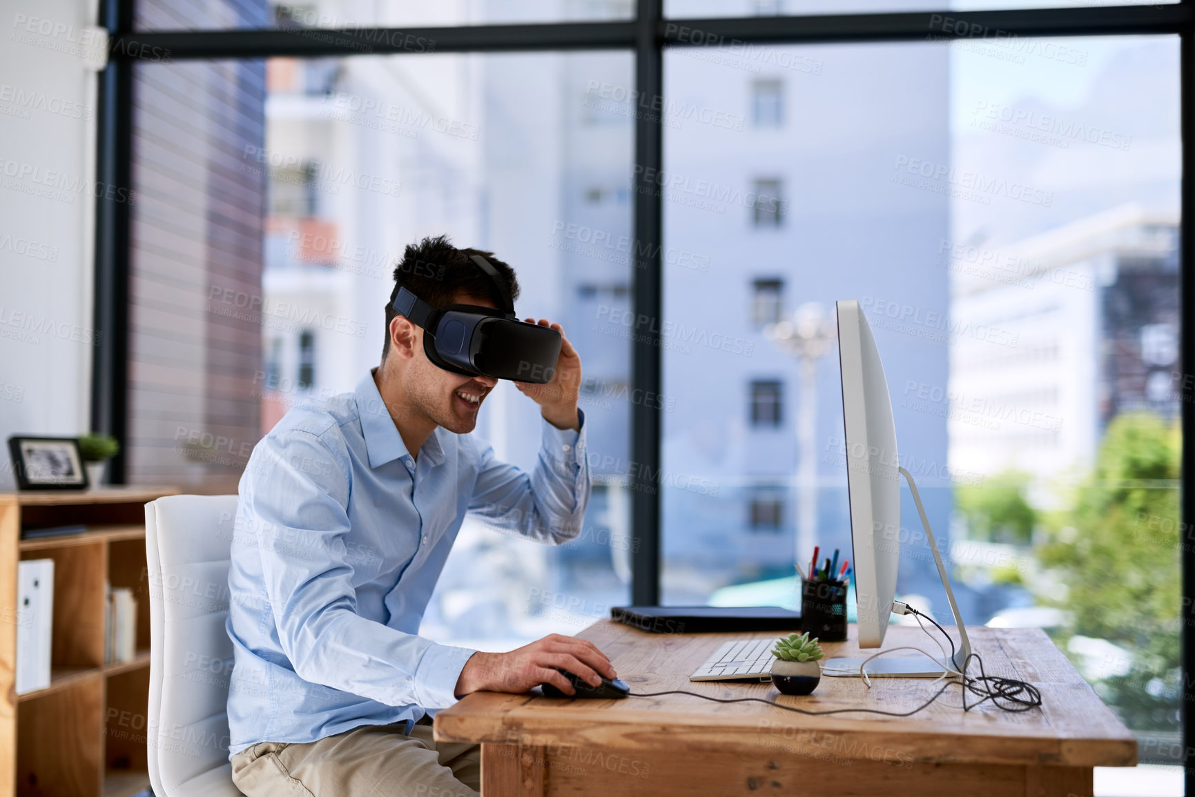 Buy stock photo Shot of a happy young businessman wearing a virtual reality headset while working at his desk in the office