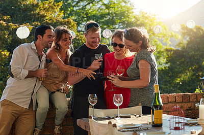 Buy stock photo Friends, phone and drinks in backyard, party and happy with video, meme or post on social media. People, men and woman with wine, alcohol and smartphone at event on mobile app in sunshine on holiday