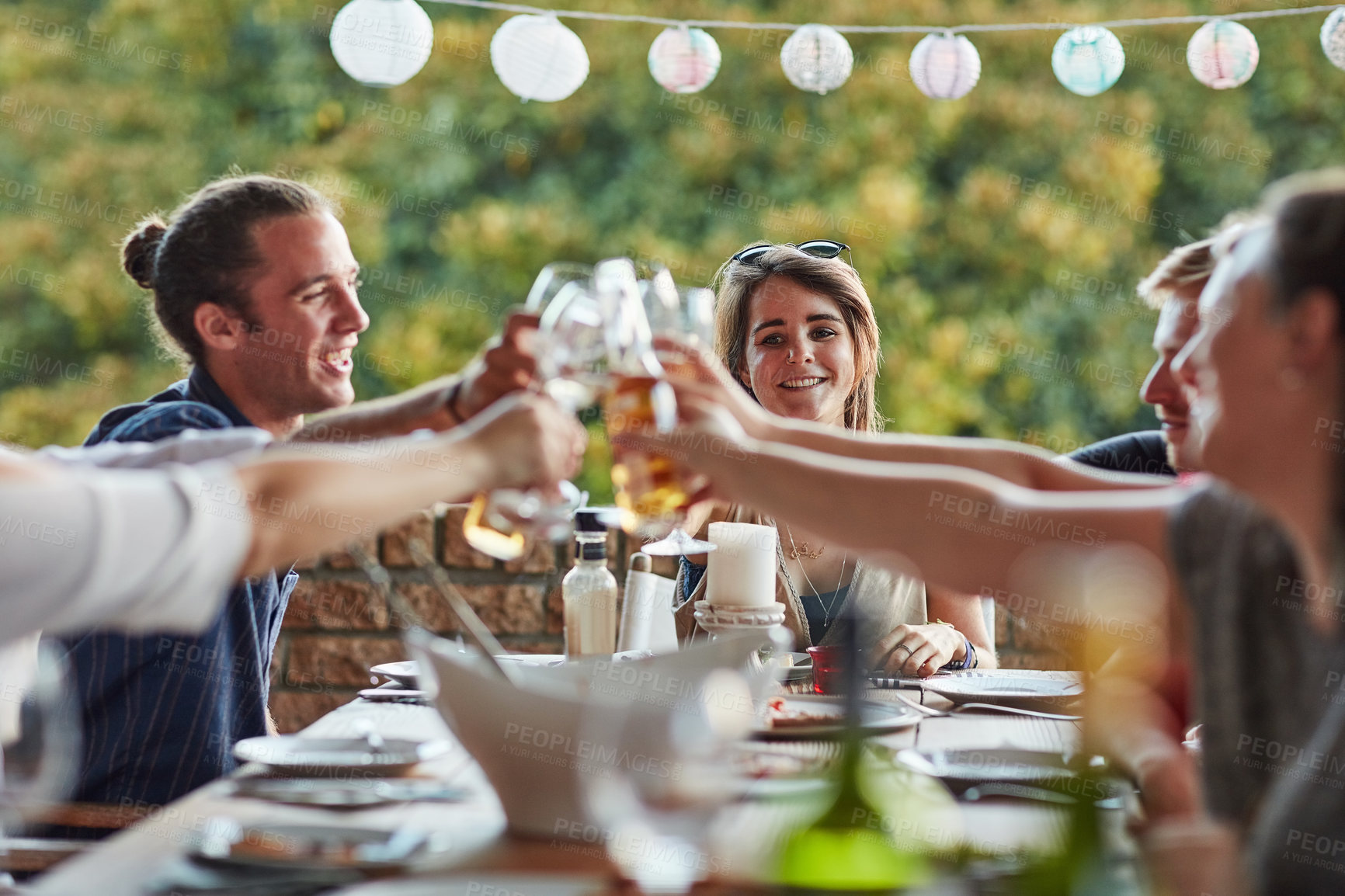 Buy stock photo Shot of a group of happy young friends toasting with wine at a backyard dinner party