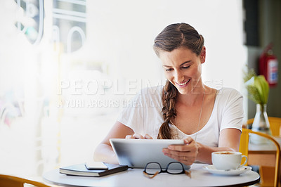 Buy stock photo Shot of a relaxed young woman using her tablet while drinking coffee at her favorite cafe