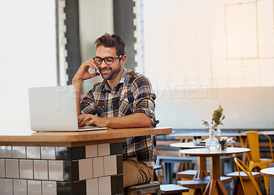 Buy stock photo Shot of a happy young entrepreneur answering his cellphone while working on his laptop in a coffee shop