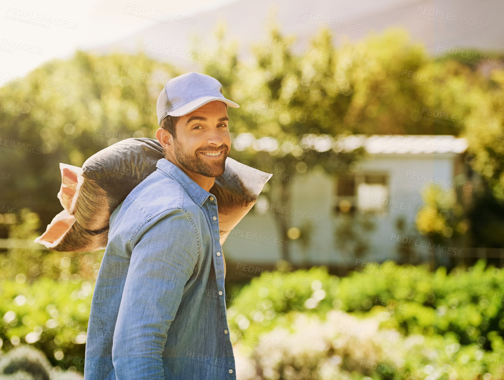 Buy stock photo Portrait of a happy young farmer carrying a bag of compost over his shoulder on the farm