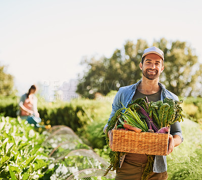 Buy stock photo Portrait of a happy young farmer harvesting herbs and vegetables in a basket on his farm