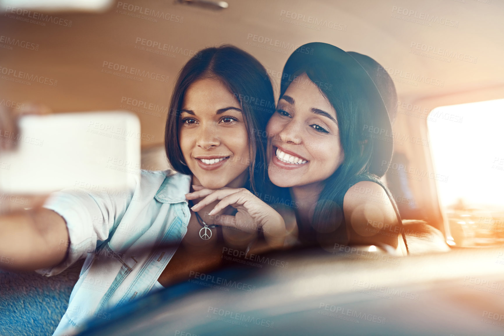 Buy stock photo Shot of two happy friends taking selfies with a mobile phone on a roadtrip