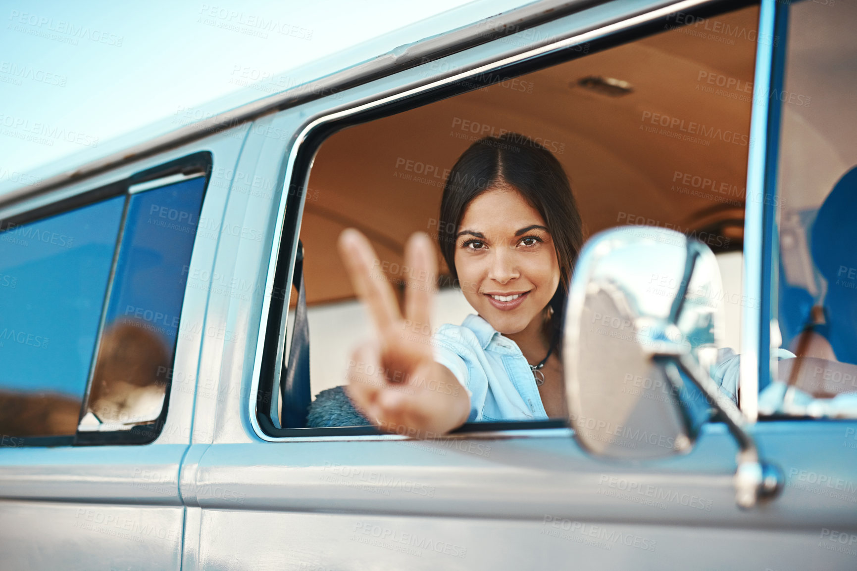 Buy stock photo Shot of a young woman leaning out of a van’s window and showing a peace sign on a roadtrip