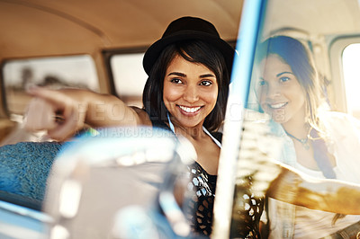 Buy stock photo Shot of a happy young woman pointing at something on a road trip with her friend