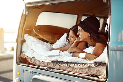 Buy stock photo Shot of  two happy friends relaxing on a blanket in the true of their van on a road trip
