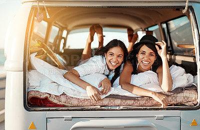 Buy stock photo Shot of  two happy friends relaxing on a blanket in the true of their van on a road trip