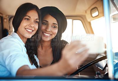 Buy stock photo Shot of two happy friends taking selfies with a mobile phone on a roadtrip