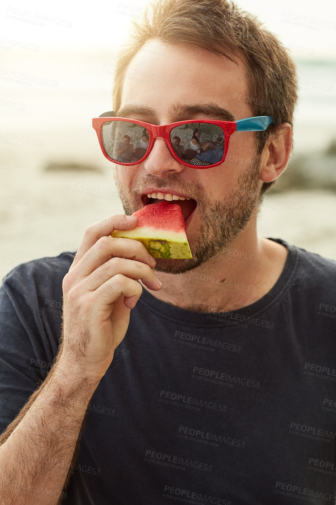 Buy stock photo Shot of a happy young man eating a slice of watermelon on the beach