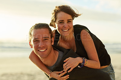 Buy stock photo Portrait of a happy young man giving his girlfriend a piggyback ride on the beach