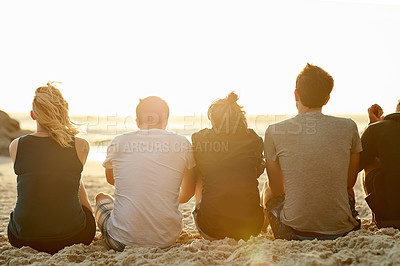 Buy stock photo Rearview shot of a group of unidentifiable friends admiring the sunset together while sitting on the beach