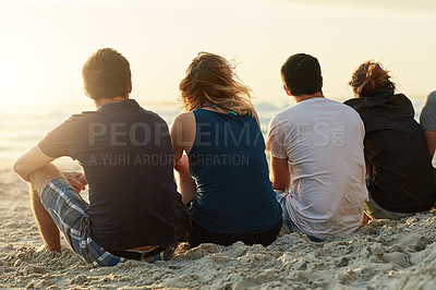 Buy stock photo Rearview shot of a group of unidentifiable friends admiring the sunset together while sitting on the beach