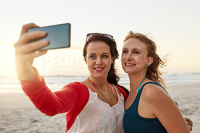 Buy stock photo Shot of two happy young friends posing for a selfie together on the beach