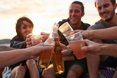 Buy stock photo Shot of a group of happy young friends toasting with their drinks while relaxing on the beach