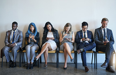 Buy stock photo Shot of a group of well-dressed businesspeople using their smartphones while waiting to be interviewed