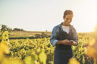 Buy stock photo Shot of a young man using his cellphone while working on a farm