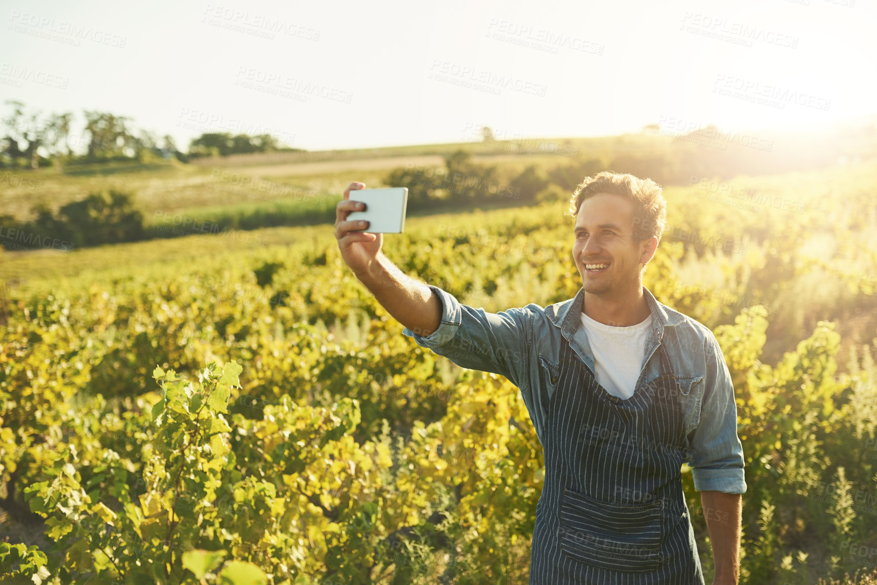 Buy stock photo Shot of a young man taking a selfie with his cellphone while working on a farm