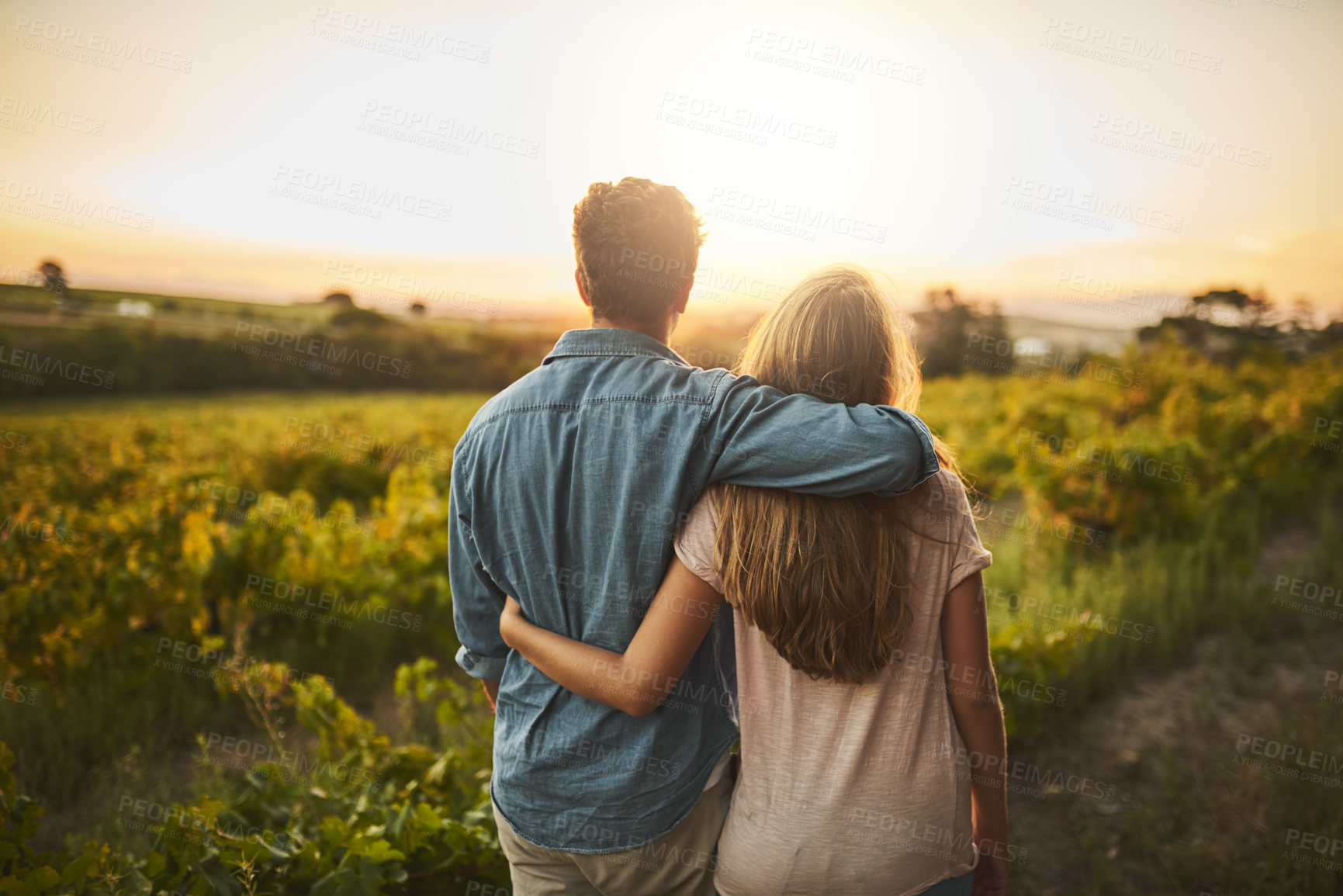 Buy stock photo Shot of a young couple walking through their crops while holding each other and looking into the horizon