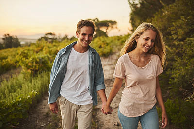Buy stock photo Shot of a young couple walking through their crops and holding hands while smiling all the way