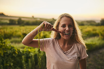 Buy stock photo Shot of a young woman holding up a carrot and taking a bite with her farmland in the background