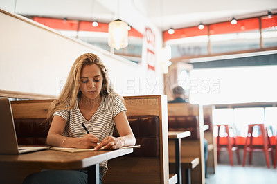 Buy stock photo Shot of a focussed young student using her laptop to study at a cafe table